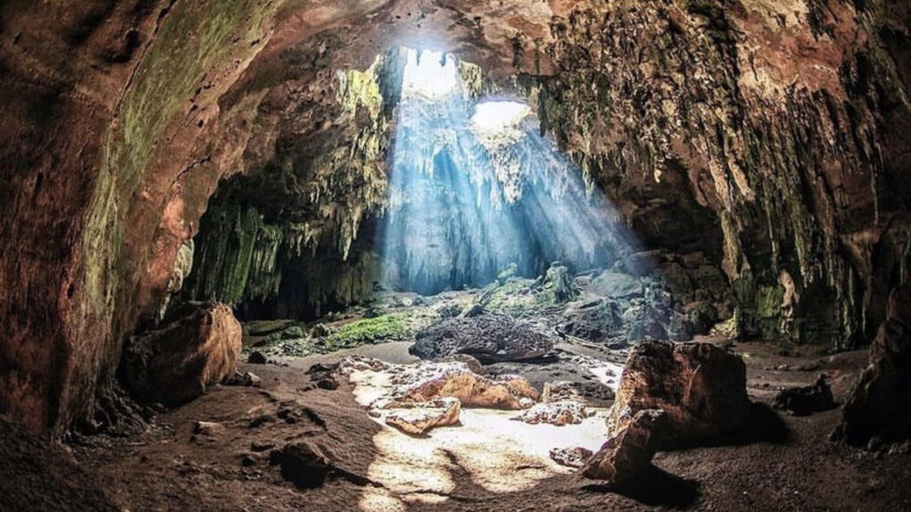 Interior de las Grutas de Loltún con formaciones rocosas y rayos de luz.